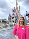 Allie Harris stands smiling in front of Disney castle at Magic Kingdom.