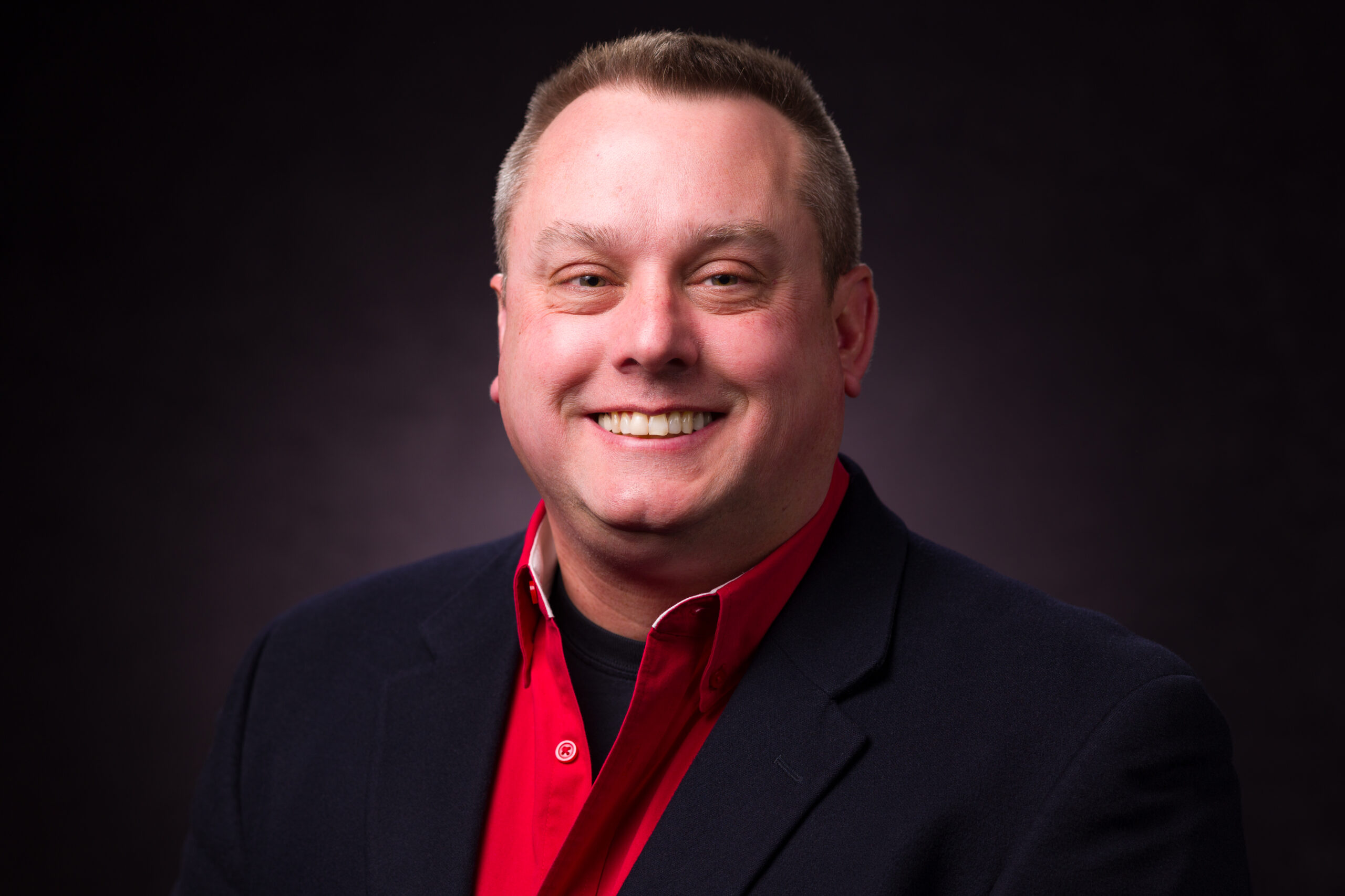 Josh Peschel in red for his headshot on a dark background