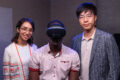 Jundi Liu research team uses virtual reality technology to study human trust of automated guided vehicles in the manufacturing setting. Photo is of three researchers in their research lab (one wearing a virtual reality headset) smiling at the camera.