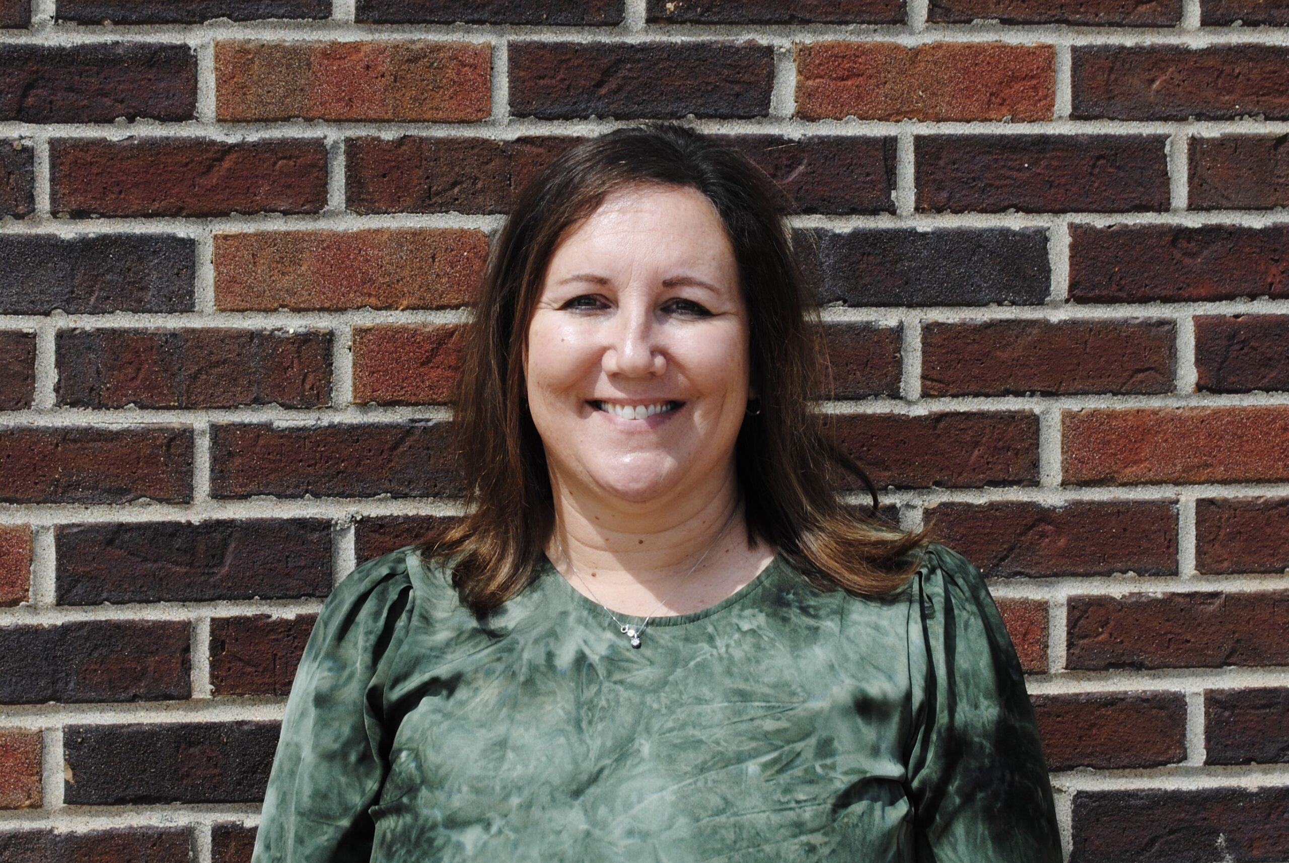 Tricia Snyder Headshot in green shirt smiling in front of red brick wall