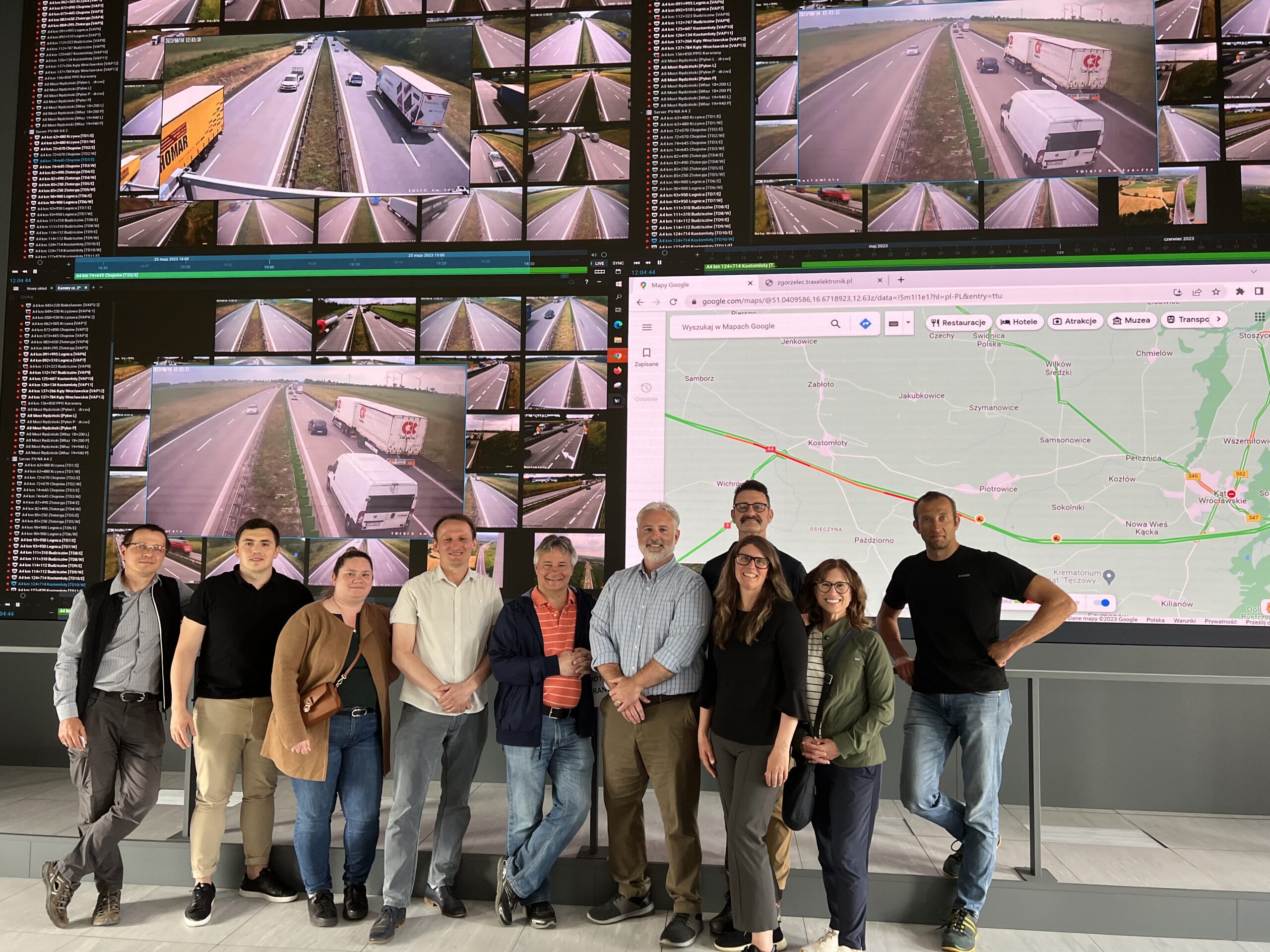 CCEE Alumni Hillary Isebrands with her team of engineers in front of four large screens depicting different roadways and maps.