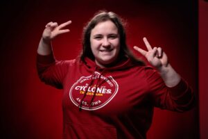 Bethany Groos, outstanding senior in biological systems engineering, holds up peace signs in front of a red background.