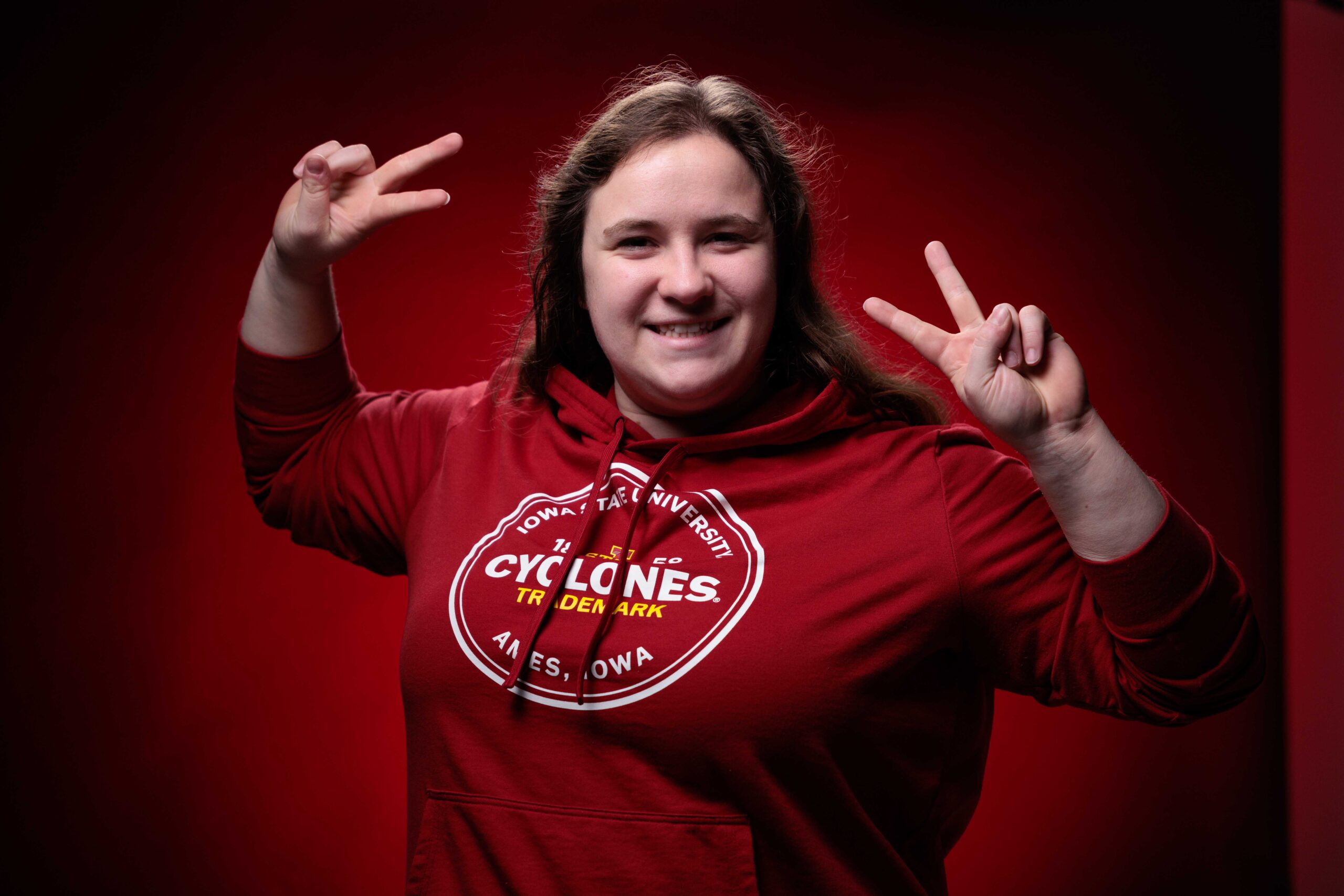 Bethany Groos, outstanding senior in biological systems engineering, holds up peace signs in front of a red background.