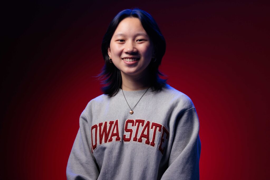 Katie Wolf: College of Engineering student marshal, computer engineering, smiles for a portrait in front of a red background.