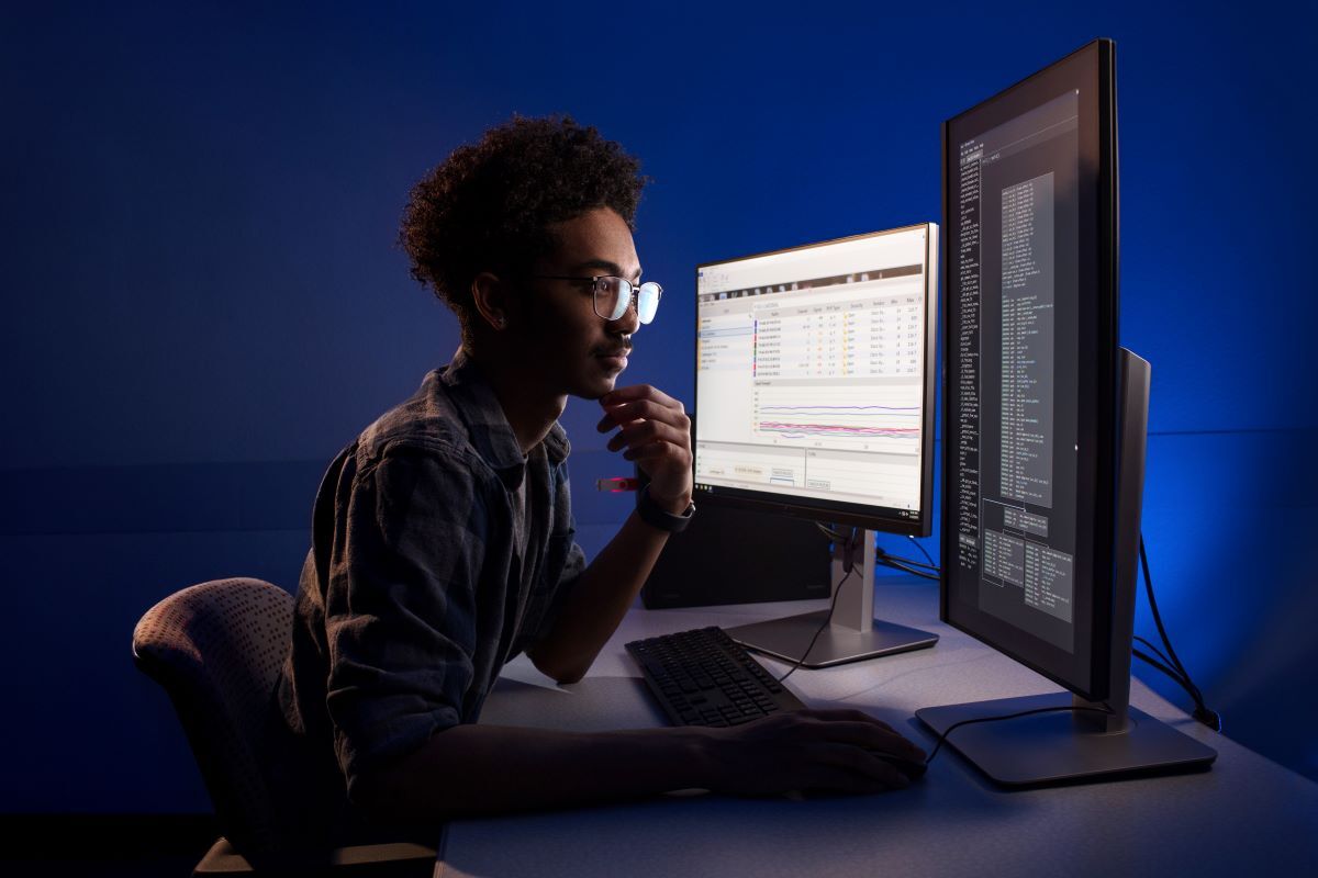 Cybersecurity student sitting at desk looking intently at computer screens