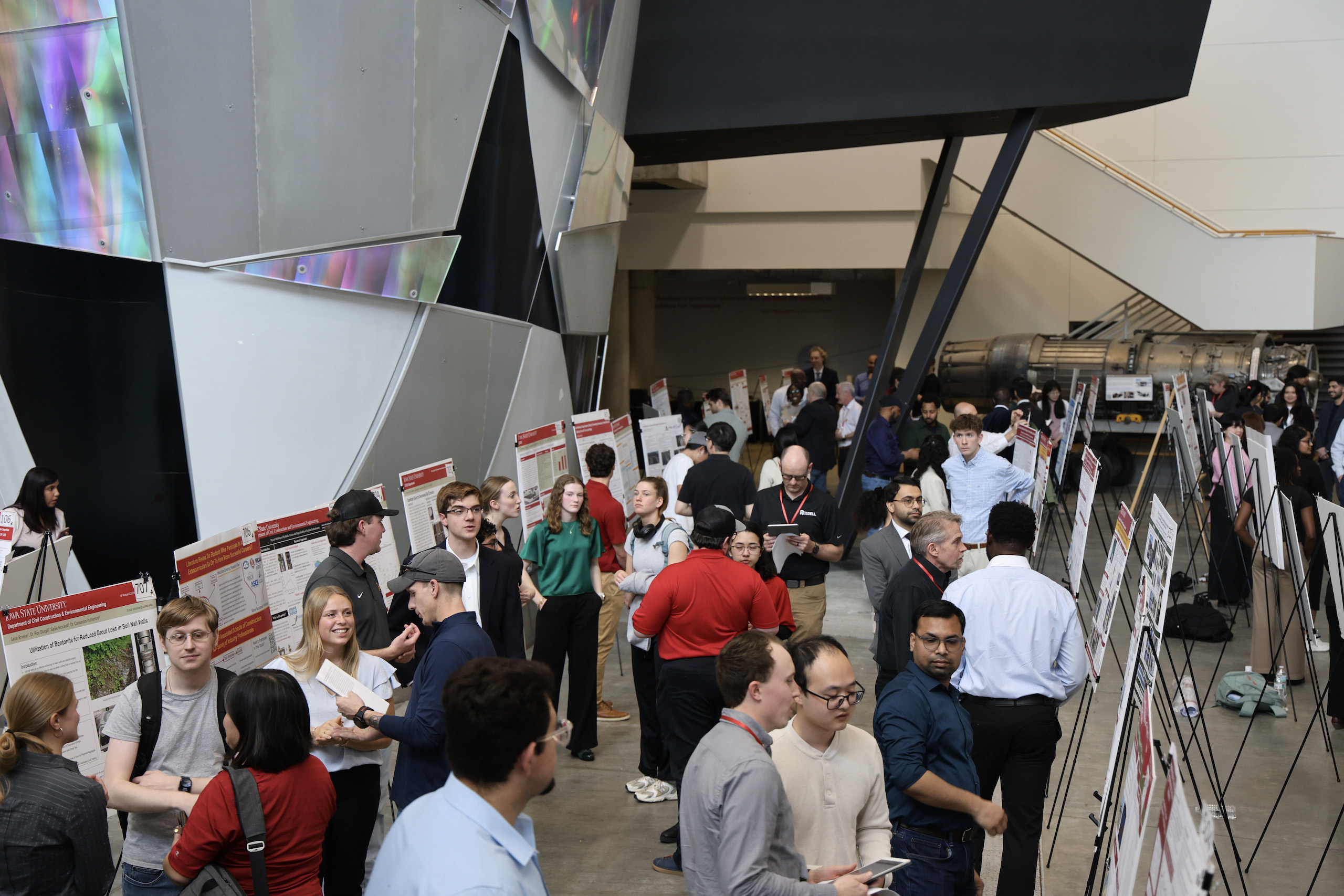 Crowded open space with research posters on easels, students crowd between the presentations.