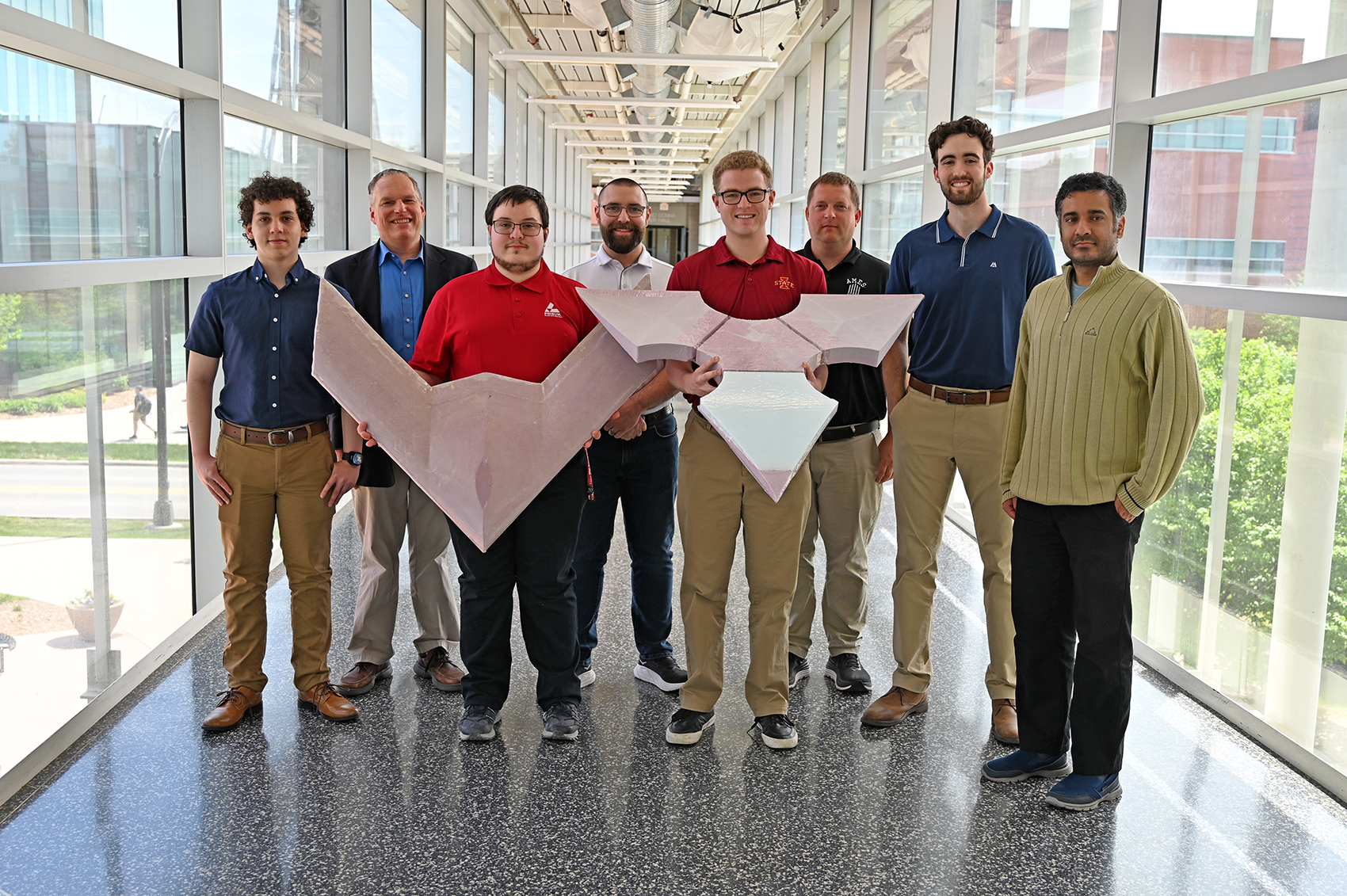IE 4530X final project team standing with two foam origami drone prototypes in the skywalk at Iowa State University.