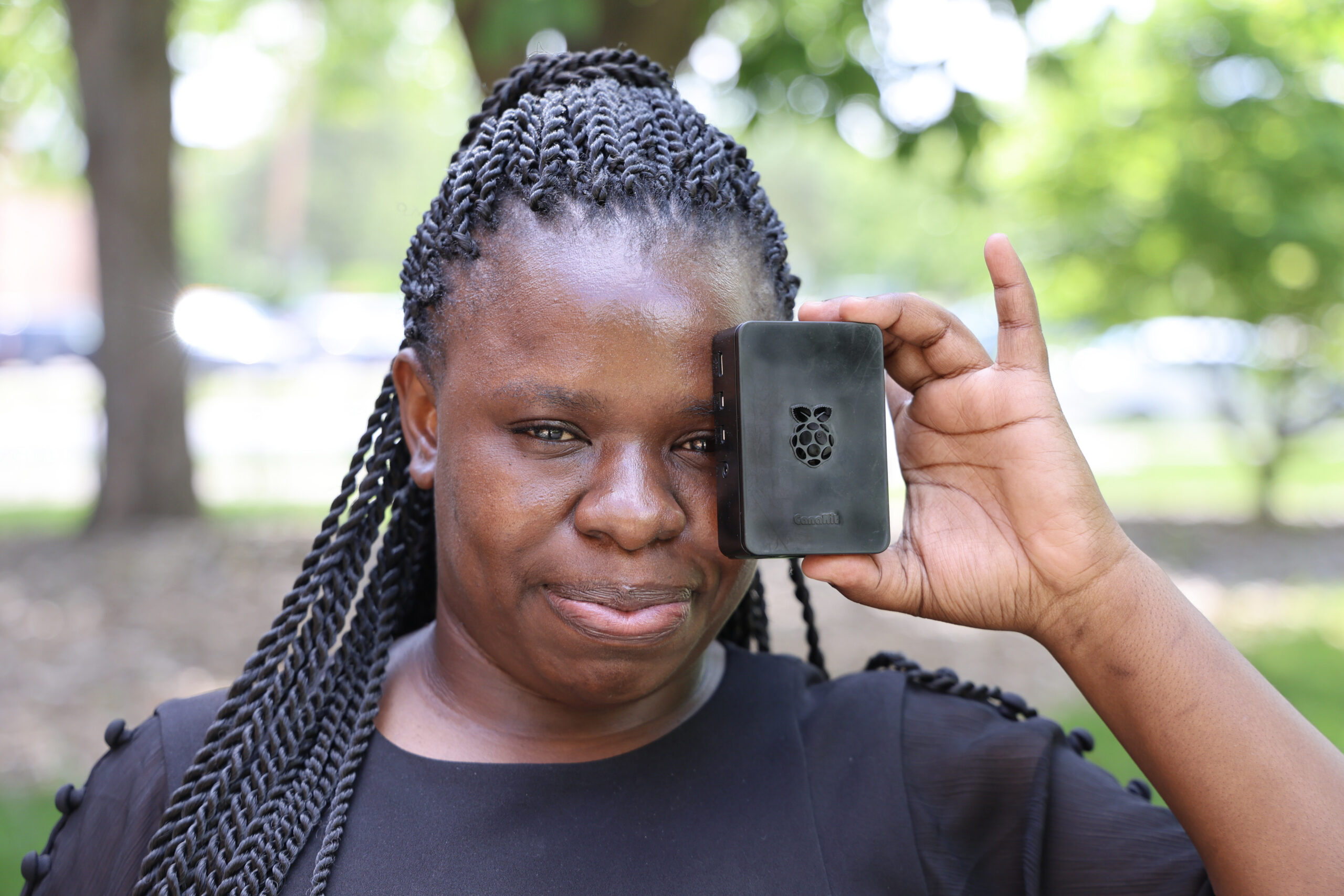 Graduate student Metrid Okumu holding, small, black, rectangle box-looking device in one hand.