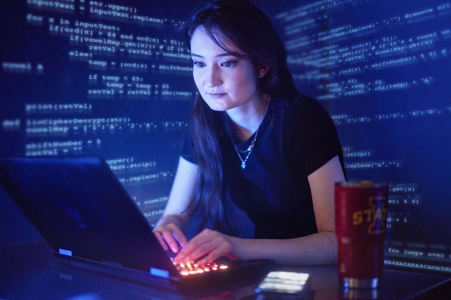 A woman works on a laptop. Computer code is shown in the background.