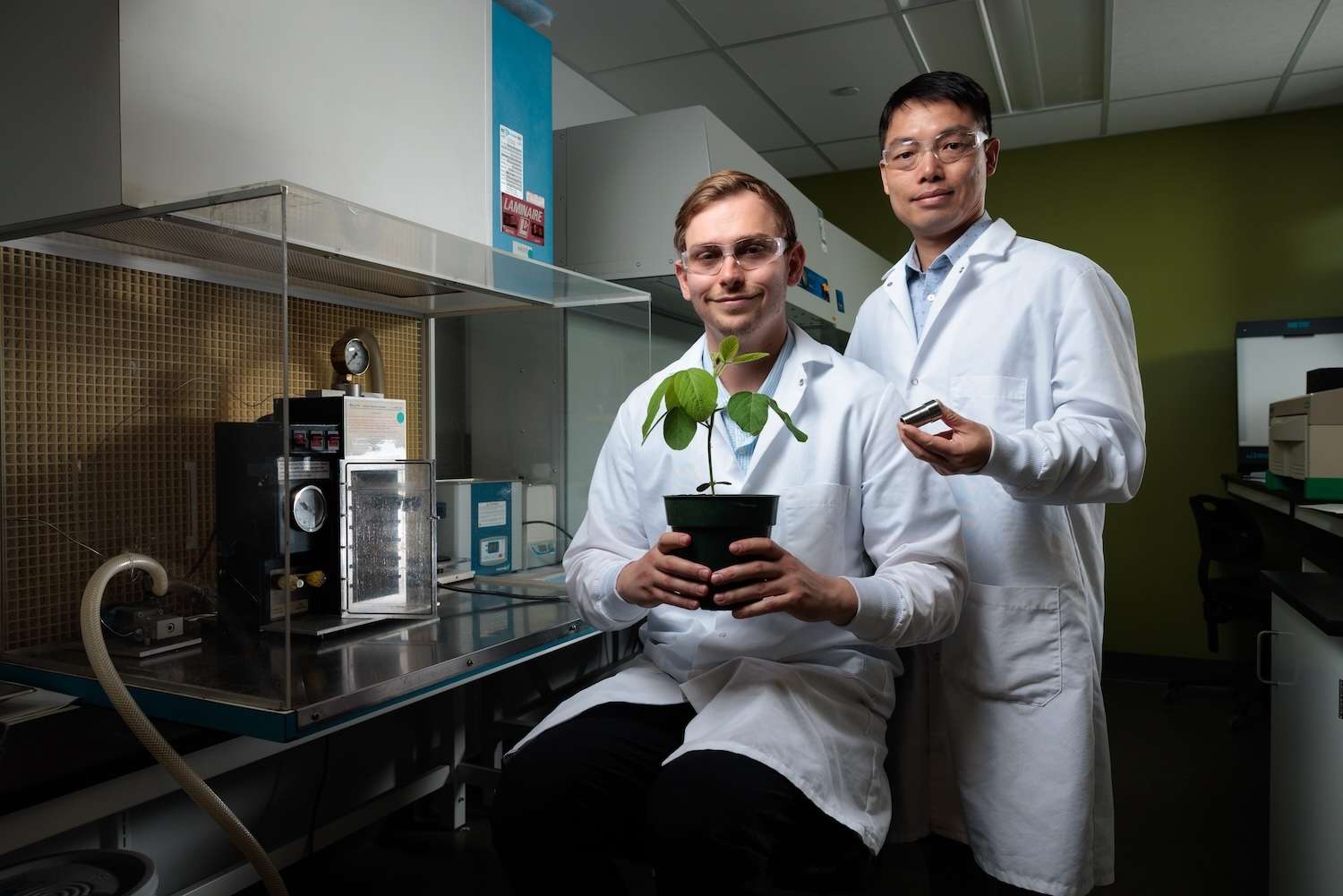 Iowa State engineers, left to right, Connor Thorpe and Shan Jiang helped invent the "Flow Guiding Barrel," which improves gene gun performance for the genetic modification of plants. Jiang is holding a Flow Guiding Barrel. A gene gun is on the left.