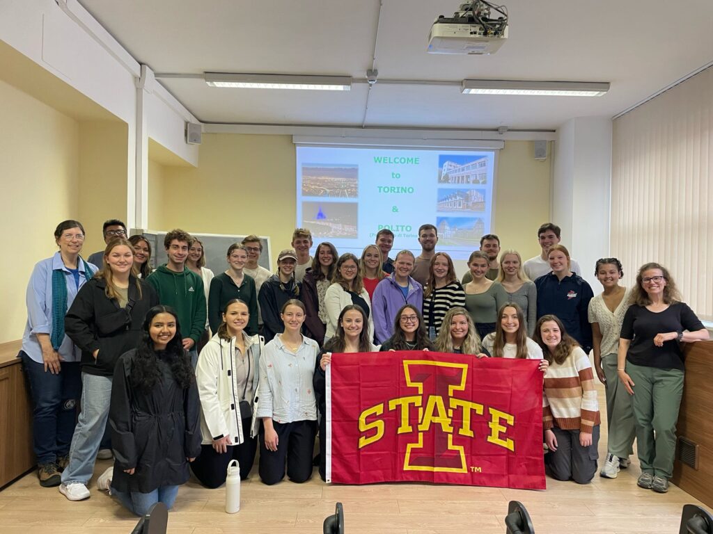 Katie Meyer and peers hold an Iowa State flag in front of a study abroad presentation.