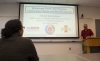 A student listens to a presentation from Dr. Subramaniam. A PowerPoint slide display's the presentation's title: Multiphase Flows: Rich Physics, Challenging Theory, and Big Simulations.
